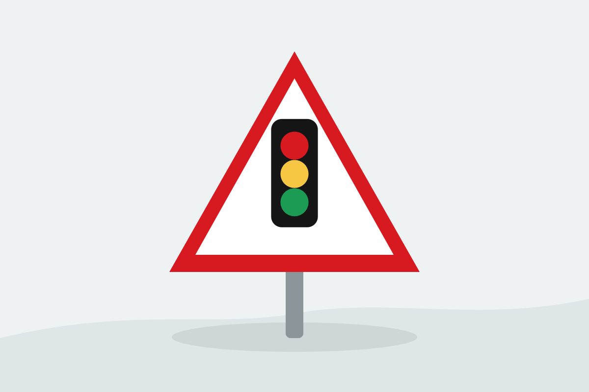 Eigenständig gezeichnetes Verkehrszeichen mit einem roten Dreieck und einem senkrechten schwarzen Gehäuse mit drei farbigen Leuchten.
