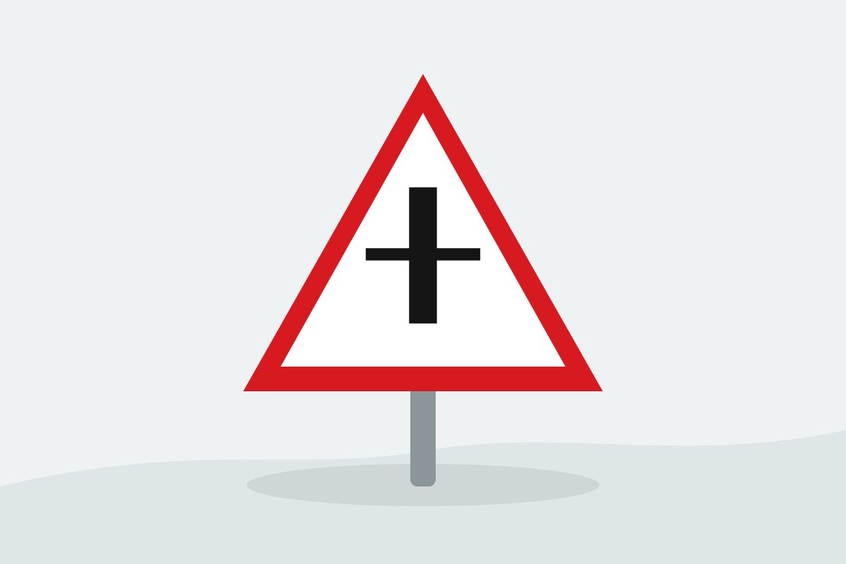 Eigenständig gezeichnetes Verkehrszeichen mit einem roten Dreieck und einer schwarzen Kreuzung mit breitem senkrechtem Hauptstrich und dünneren Querarmen.